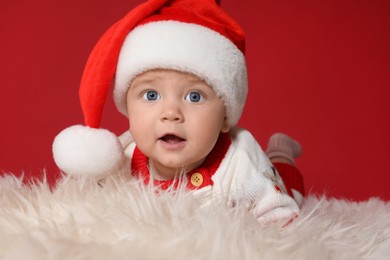 Photo of Cute baby in Santa hat on fluffy carpet against red background. Christmas celebration