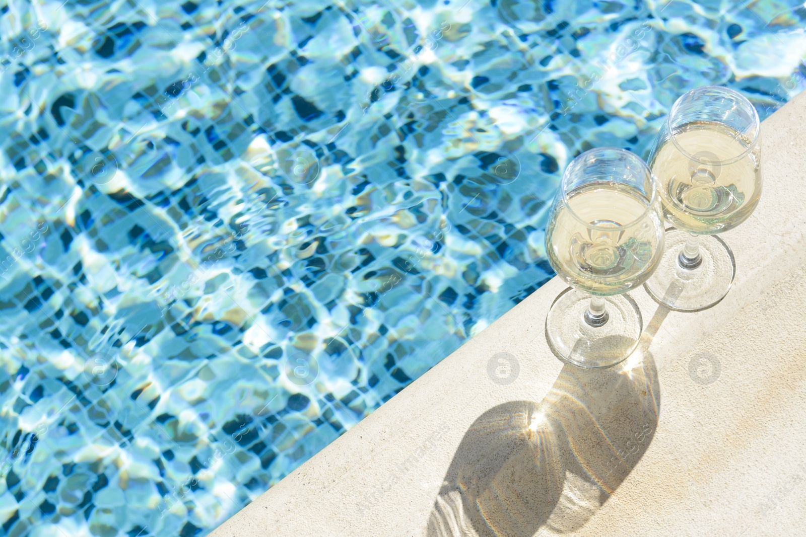 Photo of Glasses of tasty wine on swimming pool edge, space for text