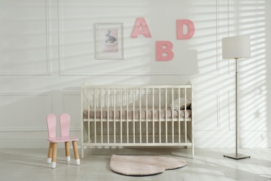 Photo of Comfortable crib near wall with pink letters in baby room. Interior design