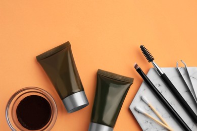Flat lay composition with eyebrow henna, professional tools and cosmetic products on orange background, space for text