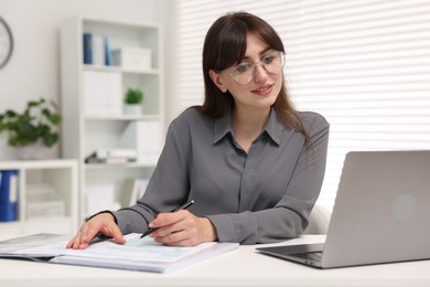 Photo of Smiling secretary doing paperwork at table in office