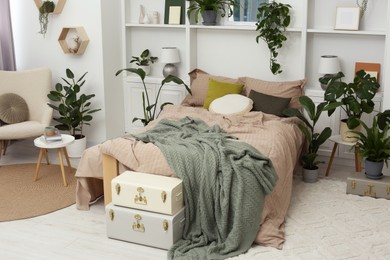 Stylish bedroom with comfortable bed and different houseplants. Interior design