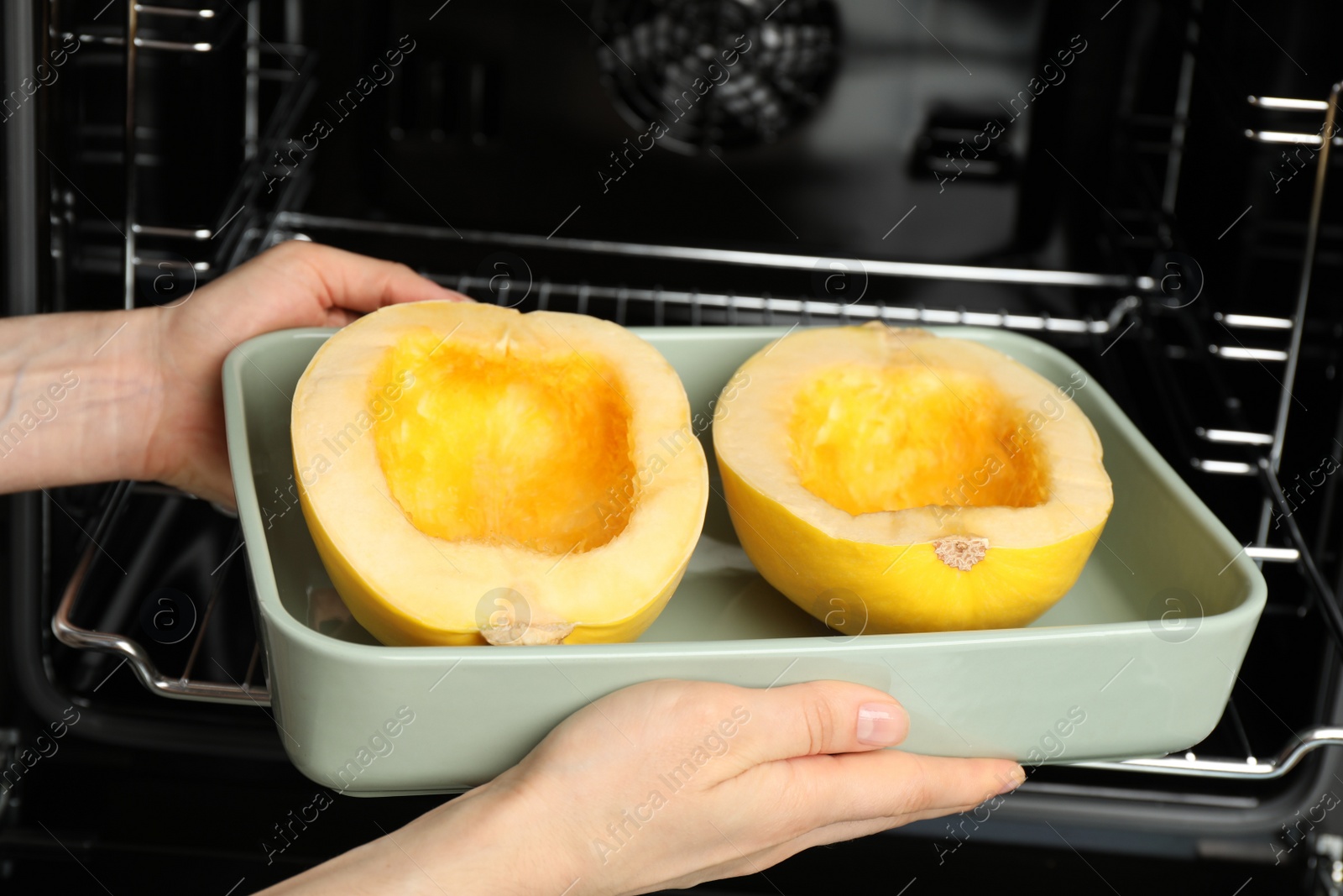 Photo of Woman putting halves of fresh spaghetti squash into oven, closeup