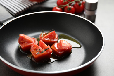 Photo of Melting ice cubes with tomatoes, oil and rosemary on grey table