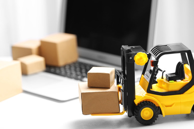 Photo of Toy forklift with boxes near laptop on table. Logistics and wholesale concept
