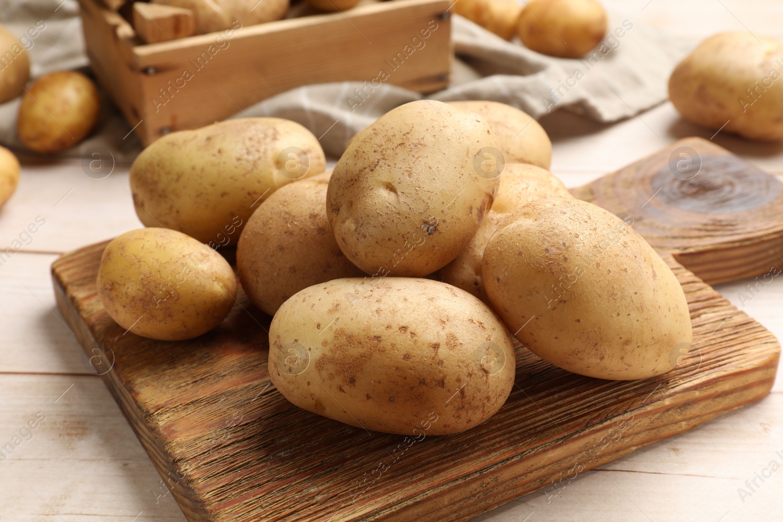 Photo of Raw fresh potatoes and cutting board on light wooden table, closeup