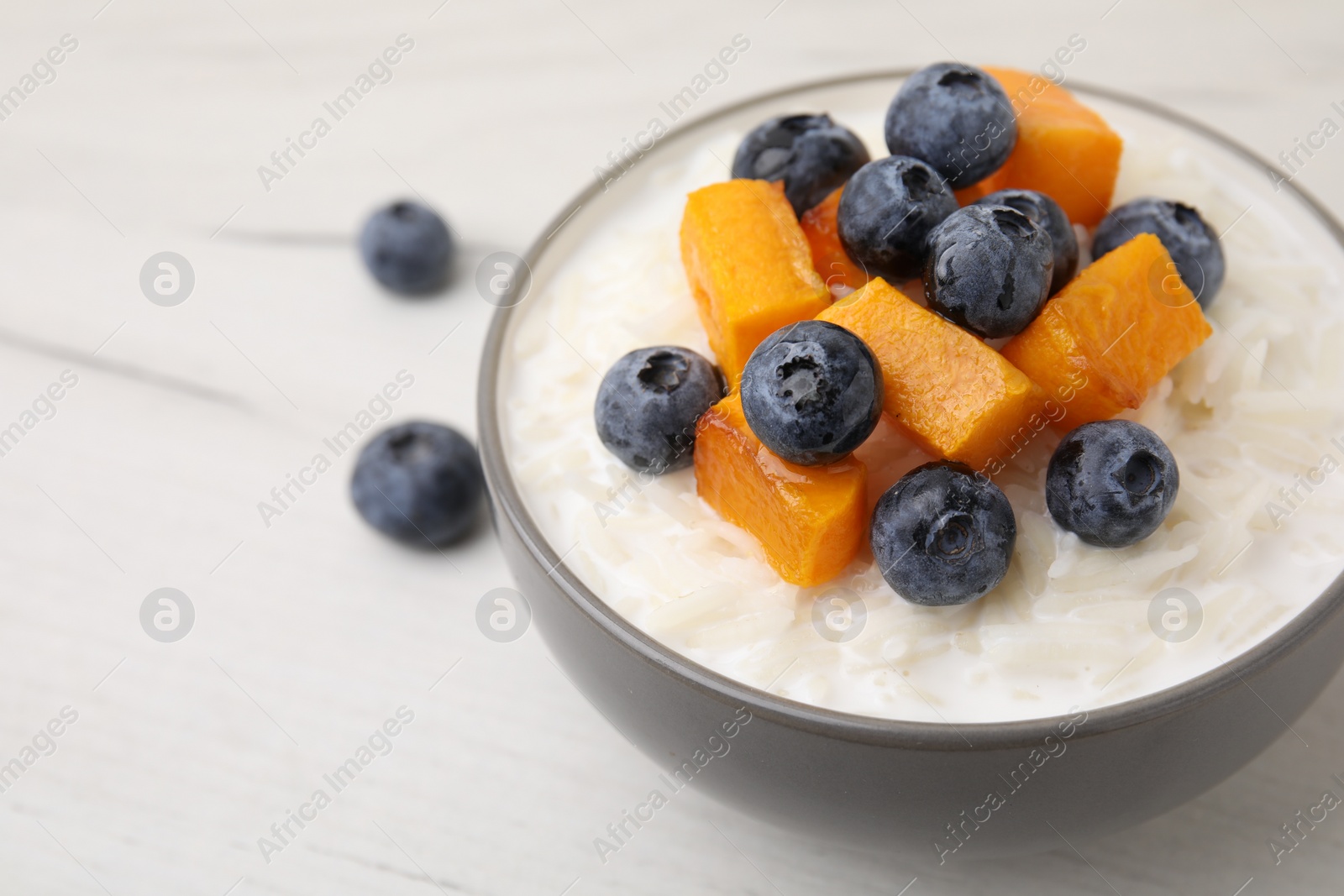 Photo of Bowl of delicious rice porridge with blueberries and pumpkin on white table, closeup