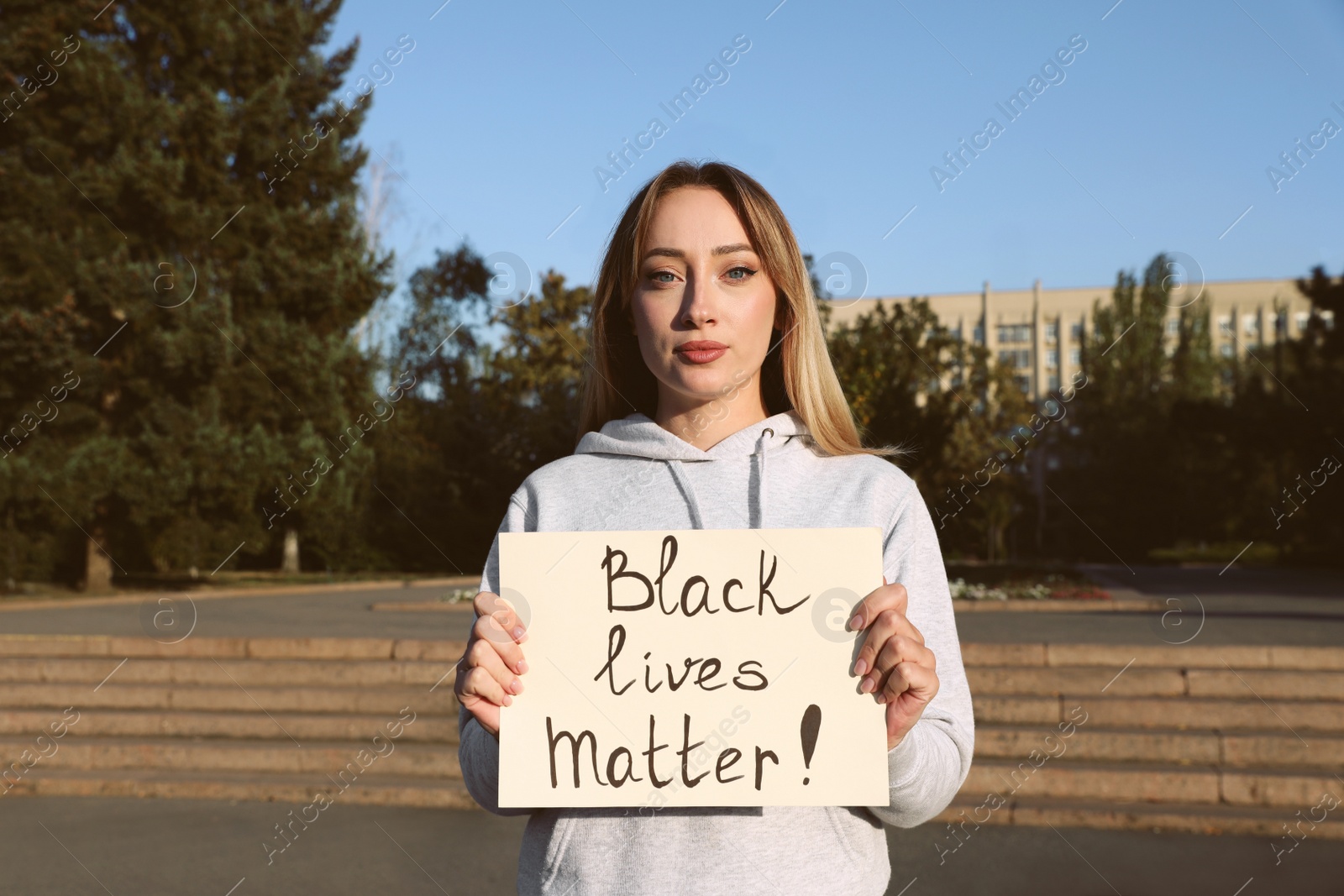 Photo of Young woman holding sign with phrase Black Lives Matter outdoors. Racism concept