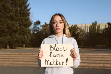 Photo of Young woman holding sign with phrase Black Lives Matter outdoors. Racism concept