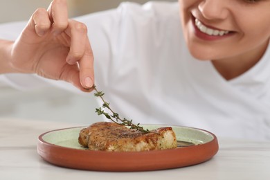 Photo of Professional chef decorating delicious meat with thyme at marble table, closeup