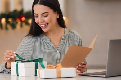 Photo of Celebrating Christmas online with exchanged by mail presents. Smiling woman opening gift box during video call on laptop at home