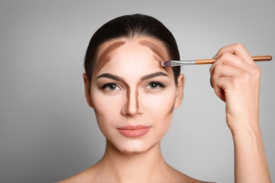 Young woman applying contouring lines on grey background. Professional makeup products