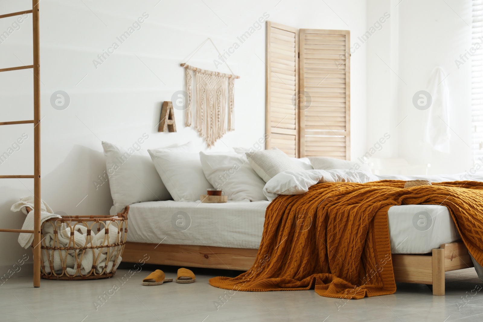 Photo of Comfortable bed with warm knitted plaid in stylish room interior