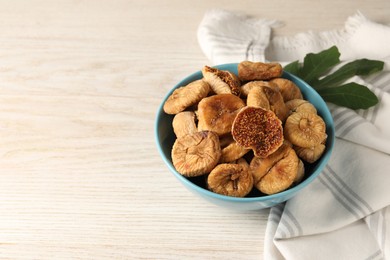 Photo of Bowl with tasty dried figs and green leaf on white wooden table. Space for text