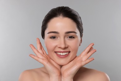 Young woman massaging her face on grey background