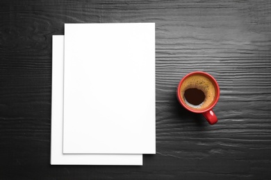 Blank paper sheets for brochure and cup of coffee on black wooden background, flat lay. Mock up