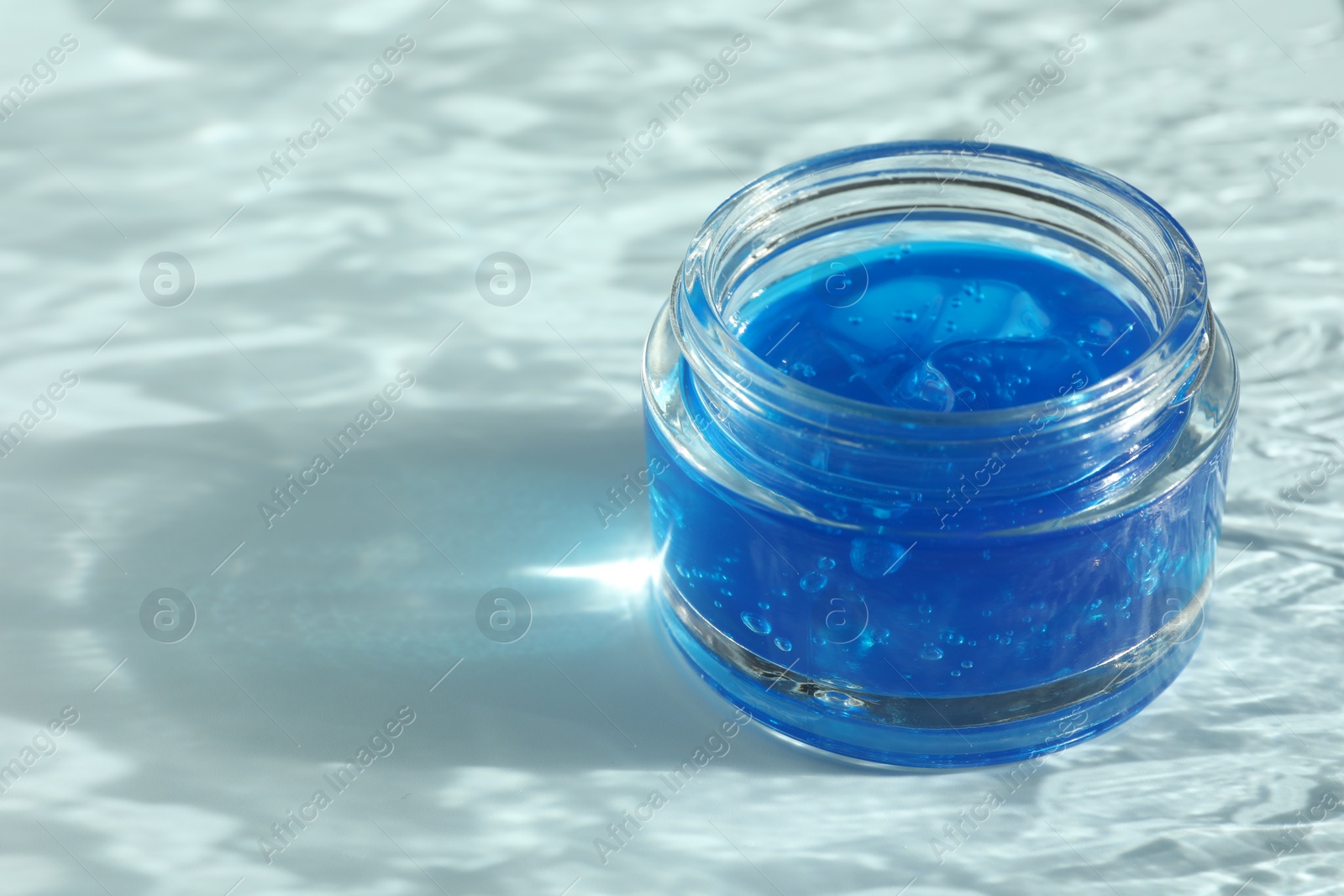 Photo of Open jar of cosmetic product on light blue background, space for text