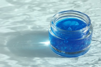Photo of Open jar of cosmetic product on light blue background, space for text
