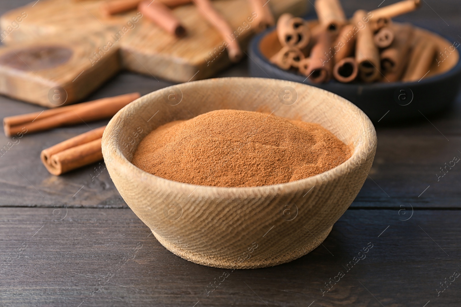 Photo of Bowl with aromatic cinnamon powder on wooden background