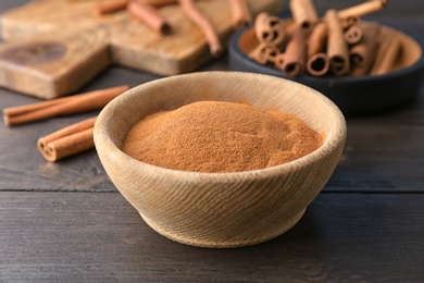 Photo of Bowl with aromatic cinnamon powder on wooden background