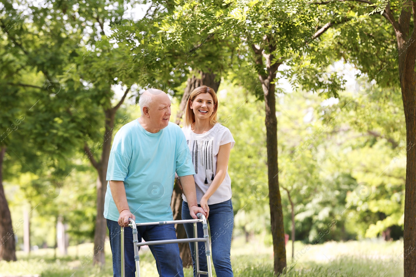 Photo of Caretaker helping elderly man with walking frame outdoors