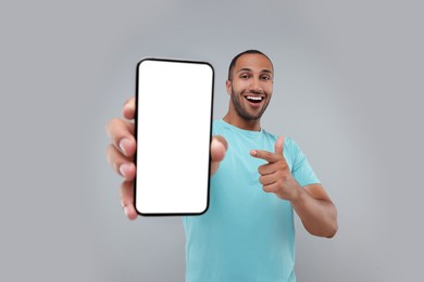 Photo of Young man showing smartphone in hand and pointing at it on light grey background