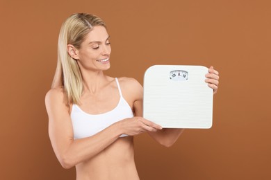 Slim woman holding scales on brown background. Weight loss