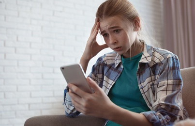 Shocked teenage girl with smartphone indoors. Danger of internet