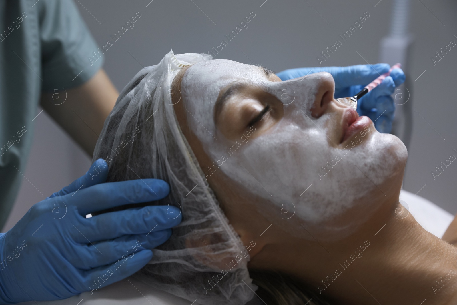 Photo of Cosmetologist applying mask on client's face in spa salon, closeup