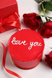 Photo of Bento cake with text Love You, gift box and roses on white wooden table. St. Valentine's day surprise