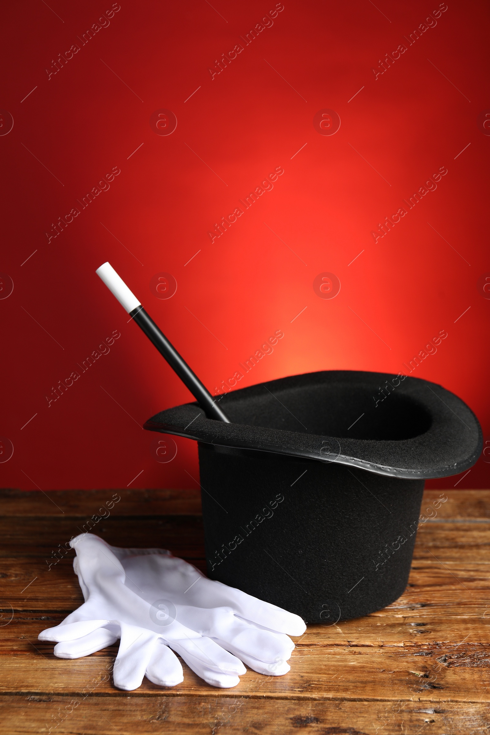 Photo of Magician's hat, gloves and wand on wooden table against red background, space for text