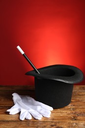 Magician's hat, gloves and wand on wooden table against red background, space for text