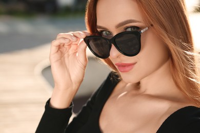 Beautiful woman in sunglasses outdoors, space for text