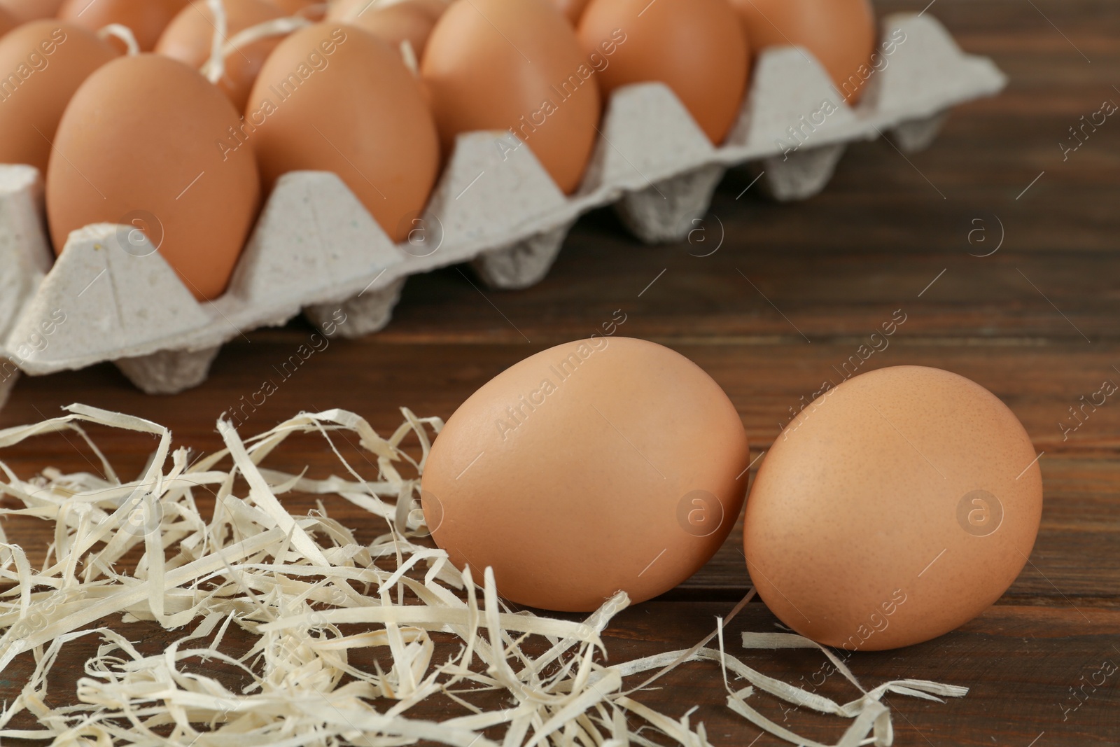 Photo of Raw brown chicken eggs and decorative straw on wooden table