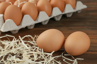 Raw brown chicken eggs and decorative straw on wooden table