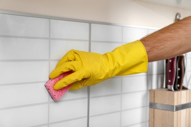 Photo of Man cleaning kitchen wall tiles with sponge, closeup