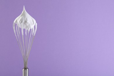 Whisk with whipped cream on violet background. Space for text