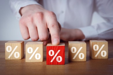 Image of Best mortgage interest rate. Man pushing red cube with percent sign on wooden table, closeup