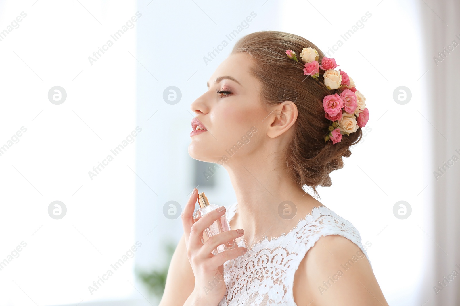Photo of Beautiful young bride with bottle of perfume on blurred background