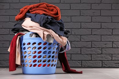 Laundry basket with clothes near black brick wall. Space for text