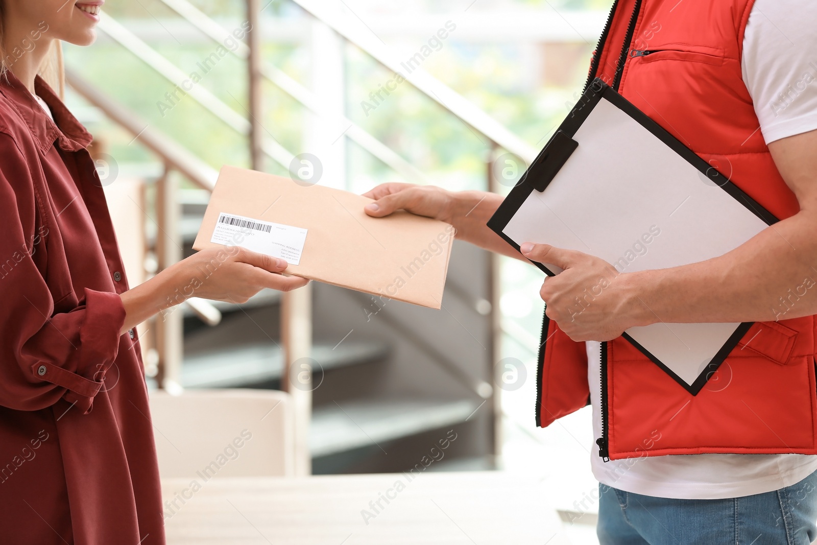 Photo of Woman receiving envelope from delivery service courier indoors