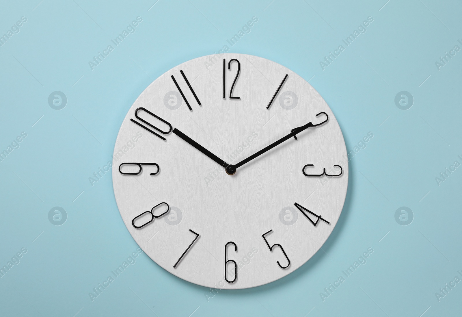 Photo of Stylish analog clock hanging on light blue wall