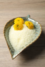 Photo of Bowl with natural sea salt and beautiful flowers on wooden table