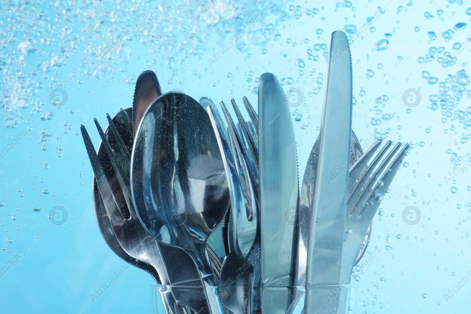 Photo of Washing silver cutlery in water on light blue background