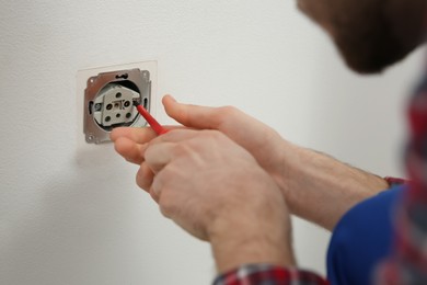 Electrician with screwdriver repairing power socket, closeup