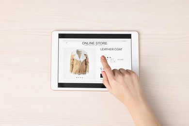 Woman with tablet shopping online at white wooden table, top view