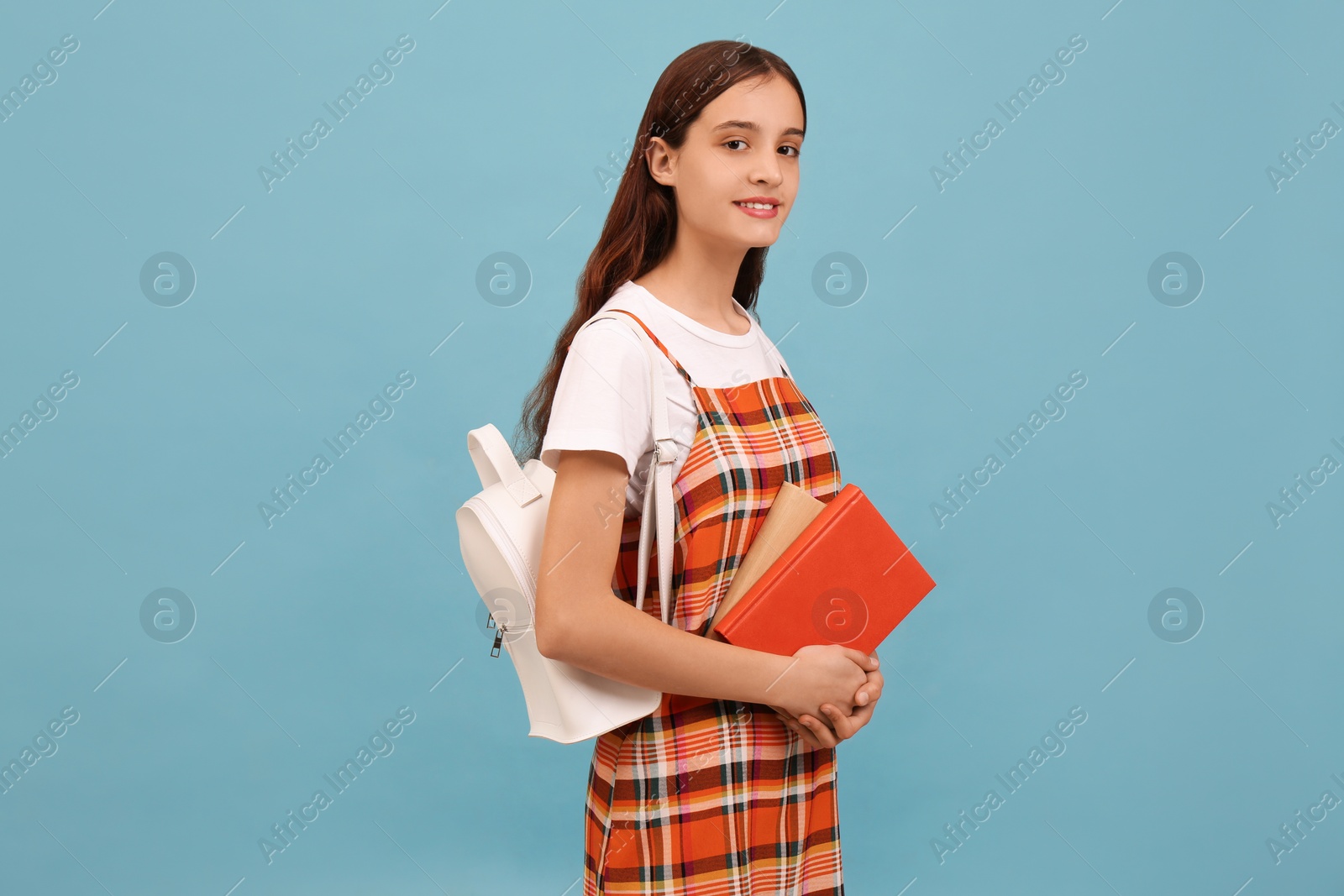 Photo of Teenage student with backpack and books on light blue background