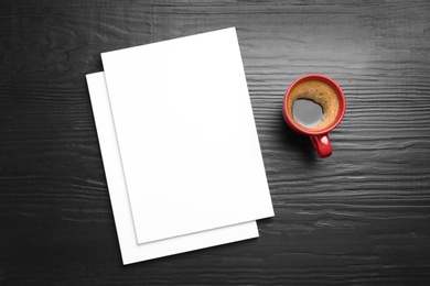 Blank paper sheets for brochure and cup of coffee on black wooden background, flat lay. Mock up