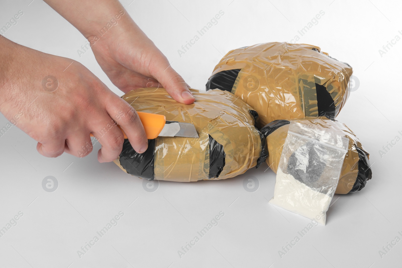 Photo of Smuggling and drug trafficking. Man opening package of narcotics with box cutter on white background, closeup