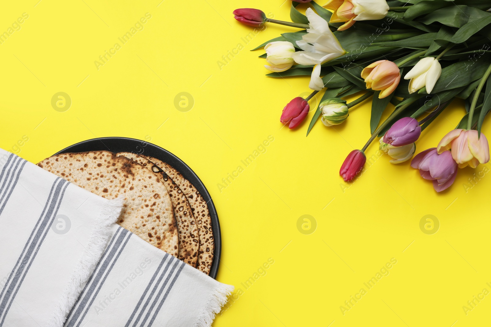 Photo of Tasty matzos and fresh flowers on yellow background, flat lay. Passover (Pesach) celebration